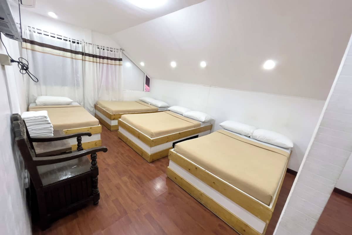 Una habitación con cuatro camas individuales, un banco de madera y una cortina.