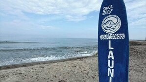 A blue surfboard with the text "LAUNION" and "DJSURF SCHOOL" on a beach. - Sebay Surf Central San Juan La Union (San Juan)