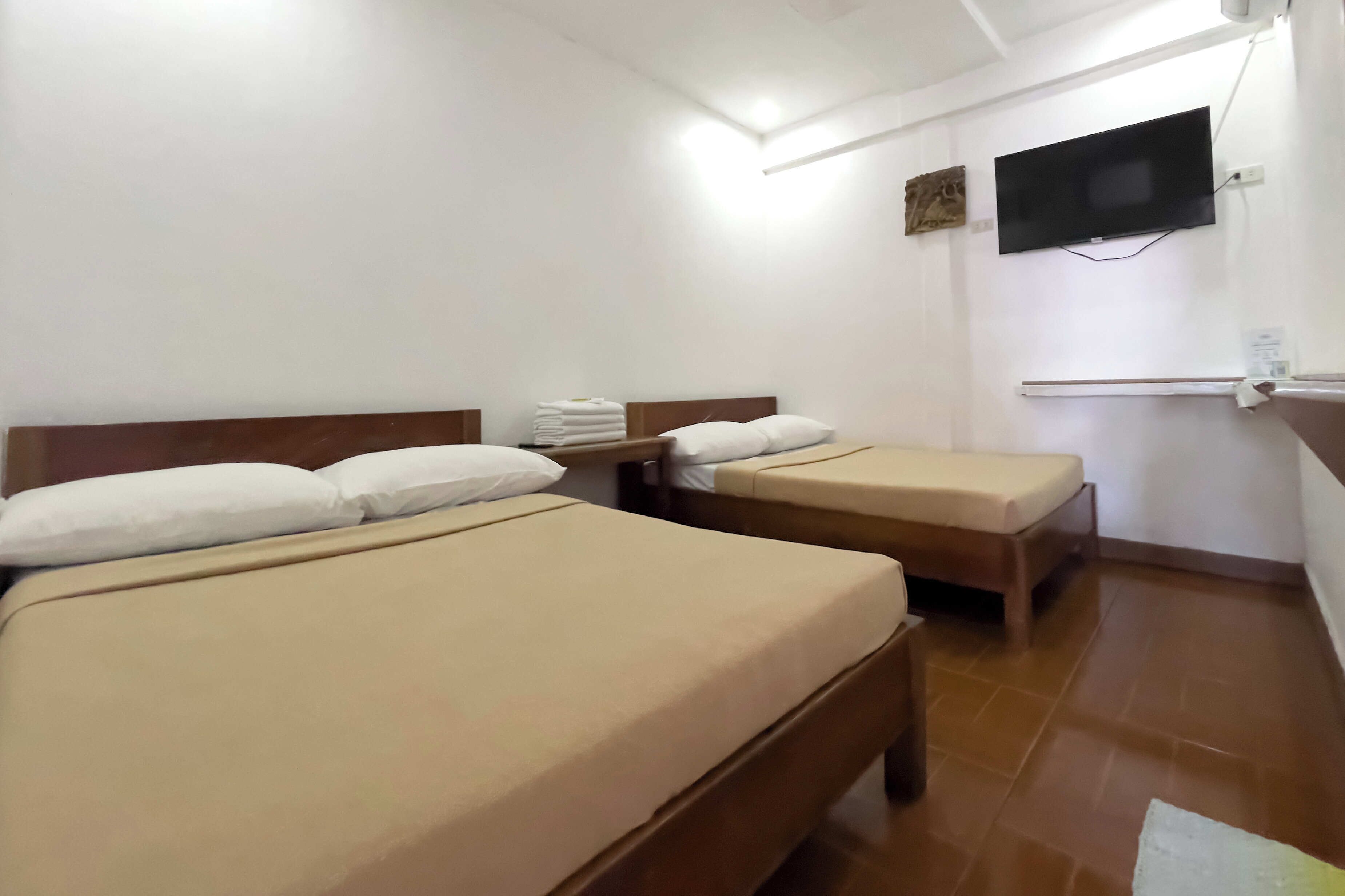Une chambre d’hôtel avec deux lits simples, un téléviseur à écran plat fixé au mur et une petite étagère avec des serviettes.