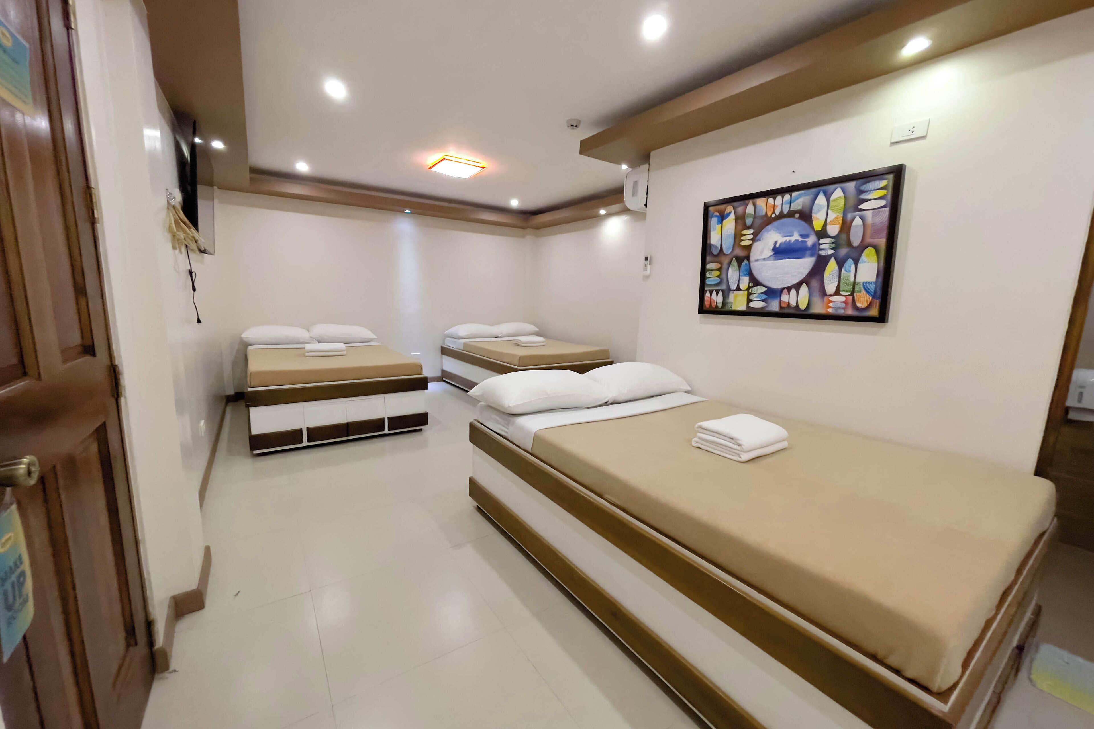 Habitación de hotel con dos camas individuales, una cama grande, un cuadro en la pared y una puerta con un letrero.