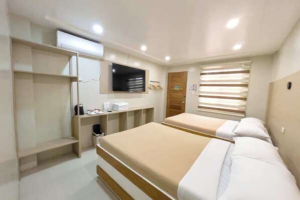 Une chambre d’hôtel avec deux lits, une télévision, une armoire et une fenêtre avec des stores.