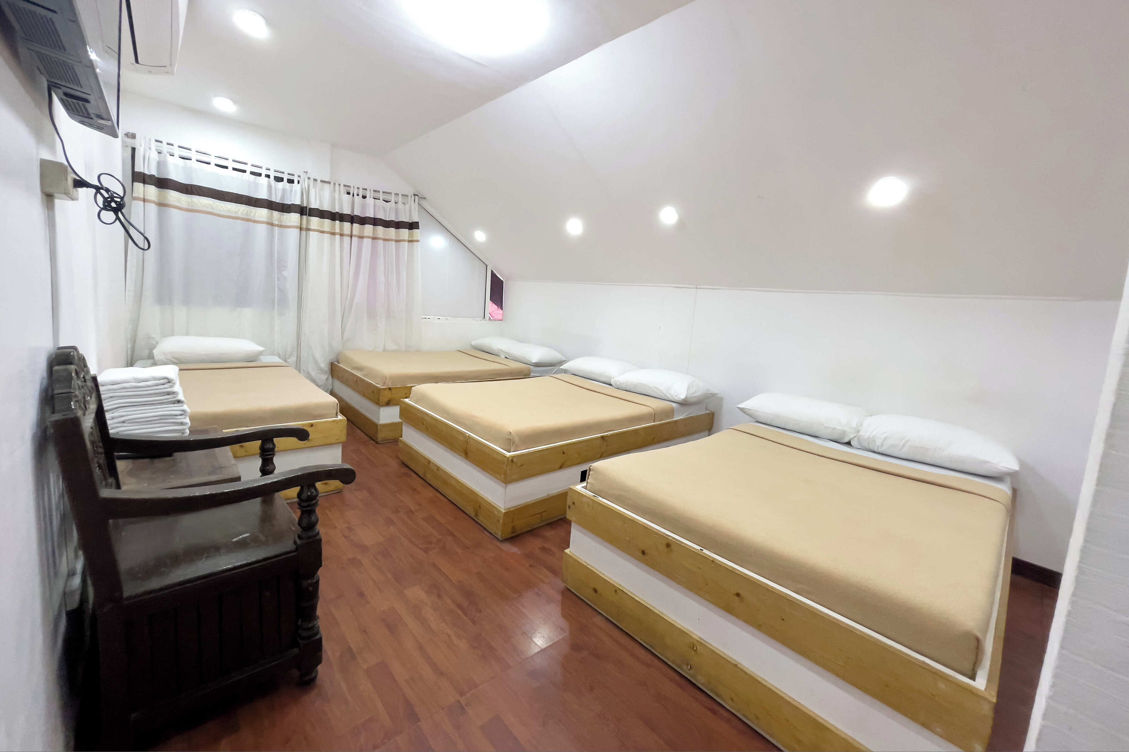 Una habitación de hotel con tres camas individuales, un banco de madera y un escritorio.