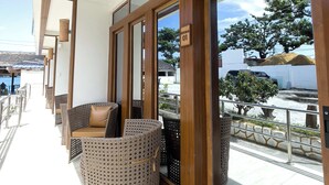 A balcony with wicker furniture, a wooden door, and a view of the street and sea. - Sebay Surf Central San Juan La Union (San Juan)