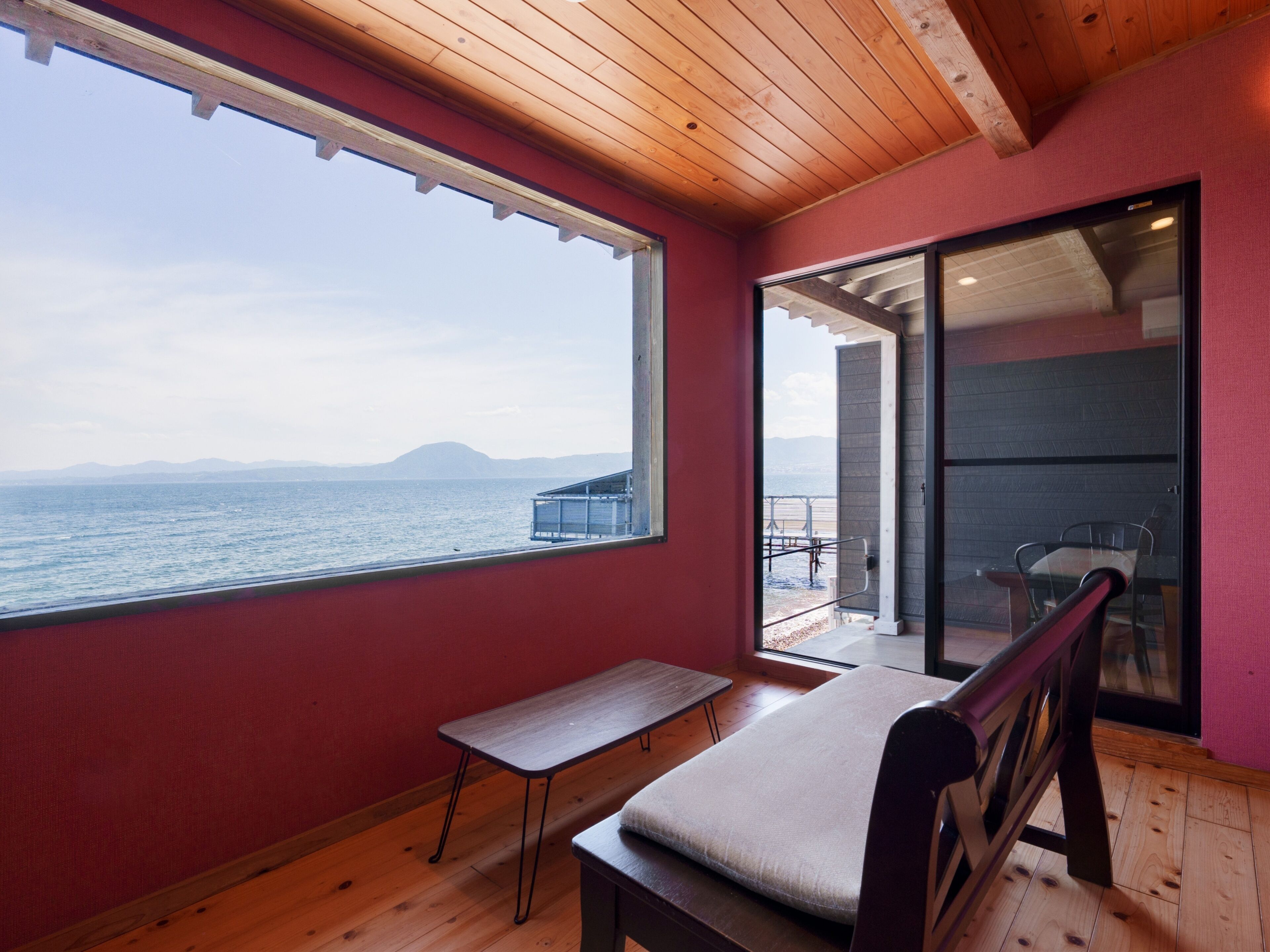 Habitación con vista al mar, un banco, una mesa y un ventanal corredera que da a un espacio exterior.