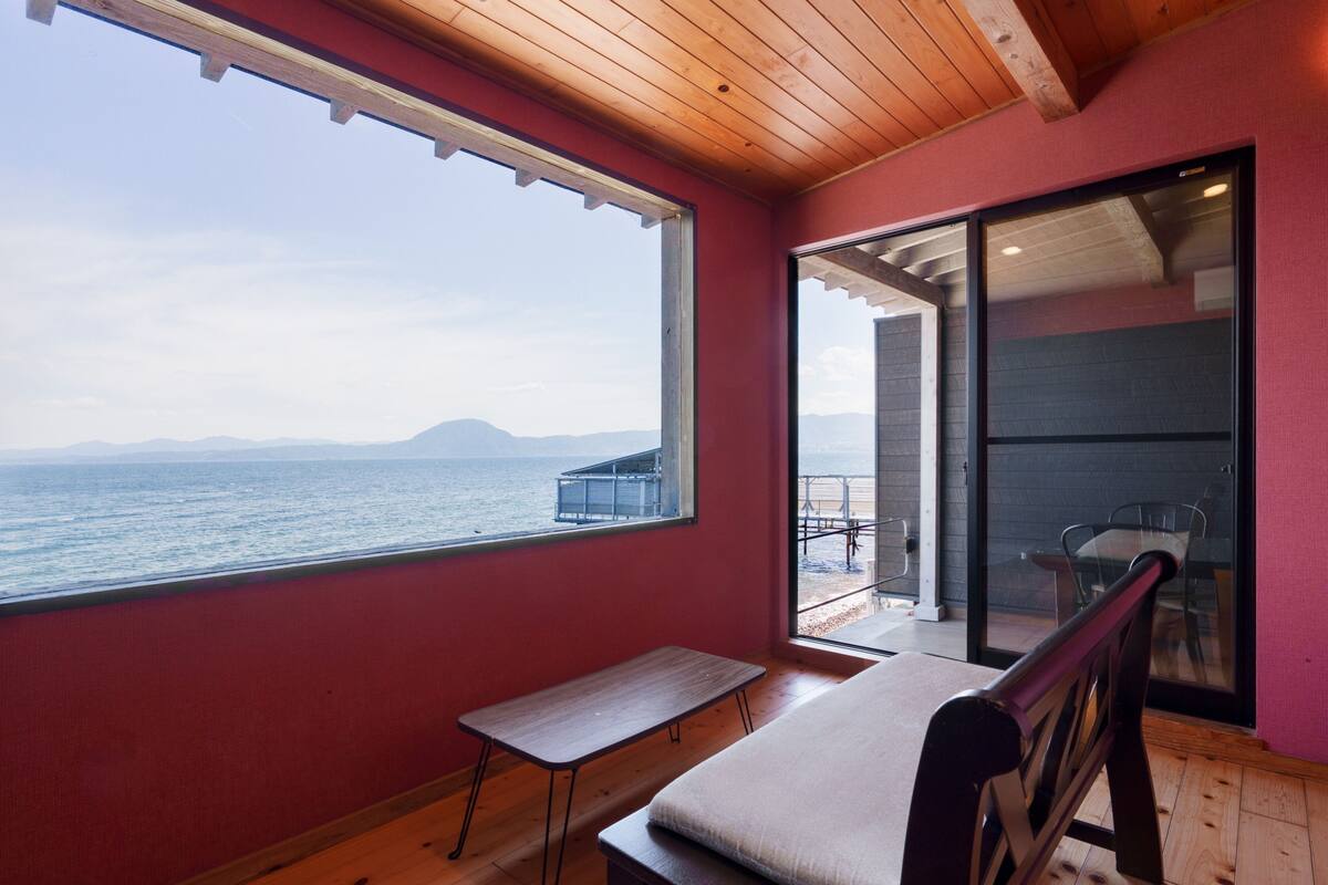 Une pièce avec vue sur la mer, un banc, une table et une porte-fenêtre coulissante donnant sur un espace extérieur.