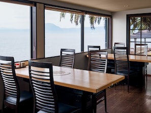 A dining area with wooden tables and chairs, large windows with a view of the sea and mountains, and a modern interior design. - costadelsol-hiji (Hiji)
