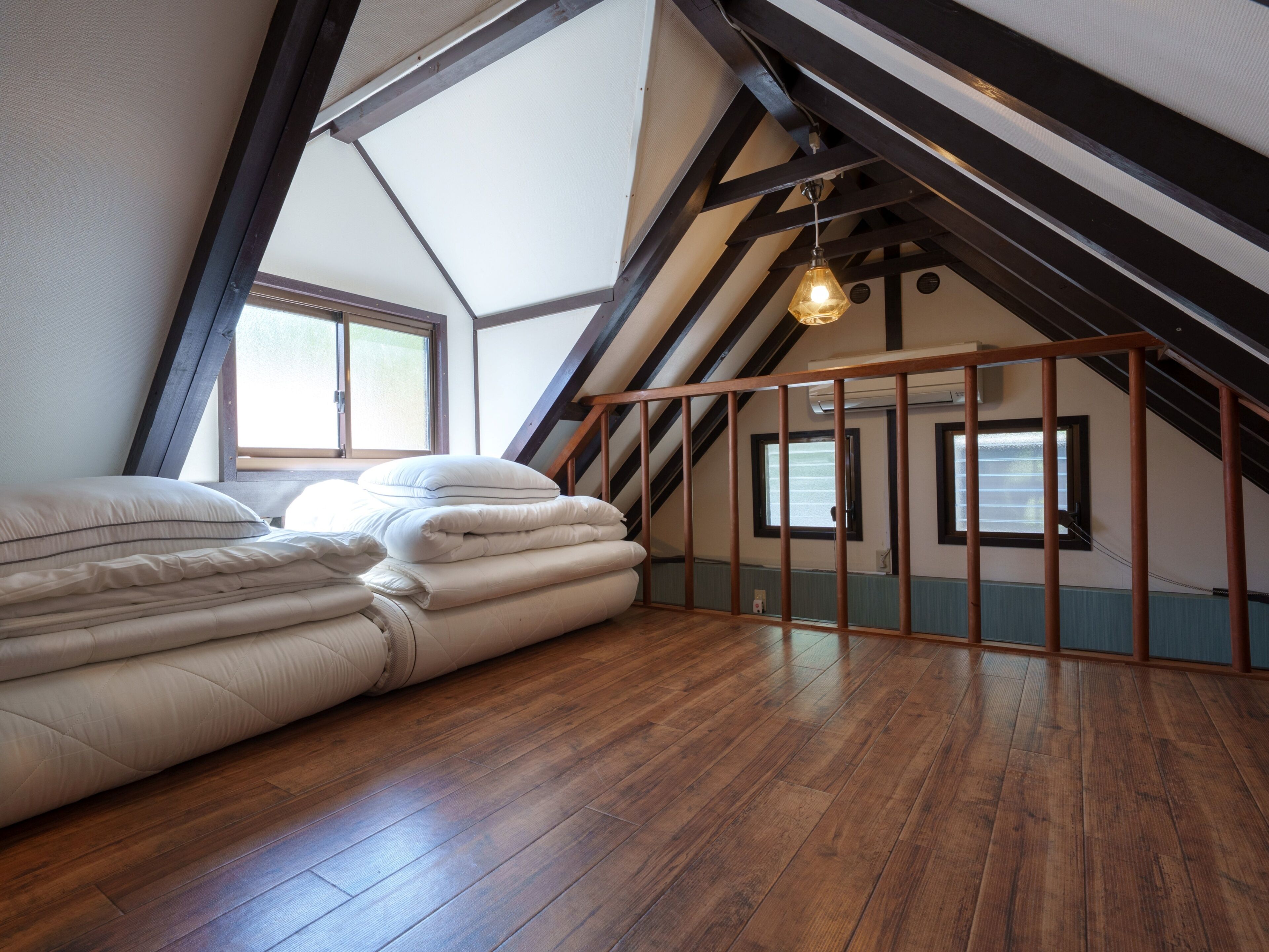 A room with a sloped ceiling, wooden beams, a bed with multiple pillows, and a hanging light fixture.