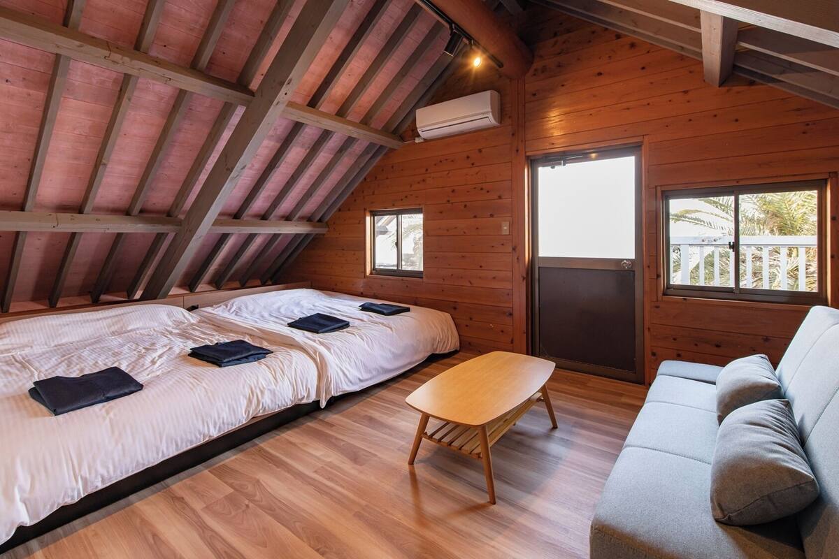 Une cabane en bois avec une chambre à coucher située en mezzanine, un canapé et une petite table.