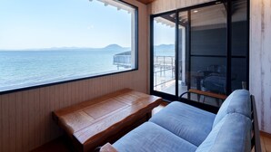A room with a wooden ceiling, a large window overlooking the sea, a wooden bench, and a sliding glass door leading to an outdoor area with a table and chairs. - costadelsol-hiji (Hiji)