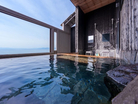A clear pool with a wooden deck, a small seating area, and a view of the sea.