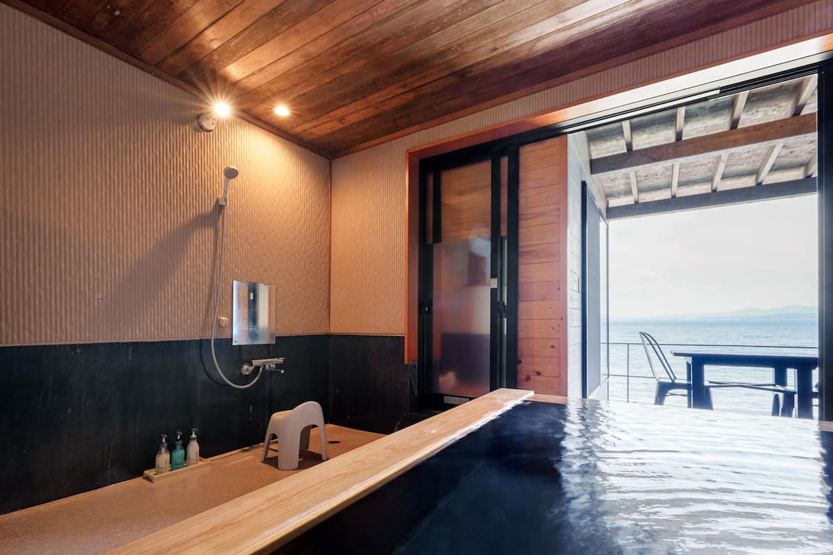 Un baño moderno con techo de madera, una bañera y vista al mar.