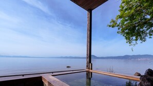 A wooden deck with a glass-bottomed hot spring pool, a stone floor, and a view of a calm body of water with distant land. - costadelsol-hiji (Hiji)