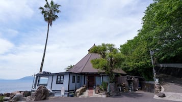 A coastal building with a tiled roof, large rocks, and a palm tree.
