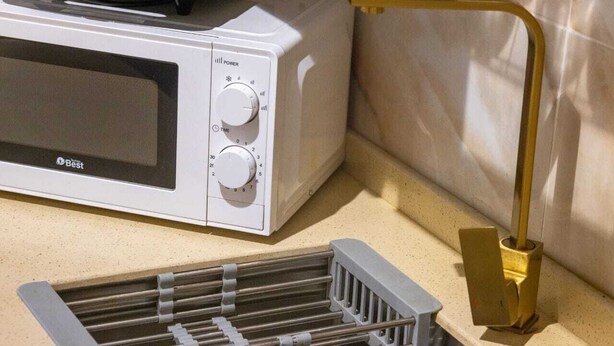 A microwave oven with a power and time dial, a gold-colored faucet, and a metal rack. - Gardenia Park Al Zahraa Serviced Apartments (Economy) (Jeddah)
