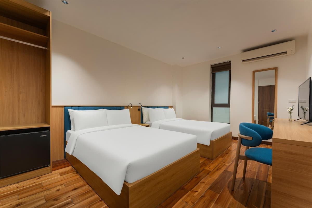Ein Hotelzimmer mit zwei Betten, einem Schreibtisch, einem Stuhl und einer kleinen Küchenzeile.