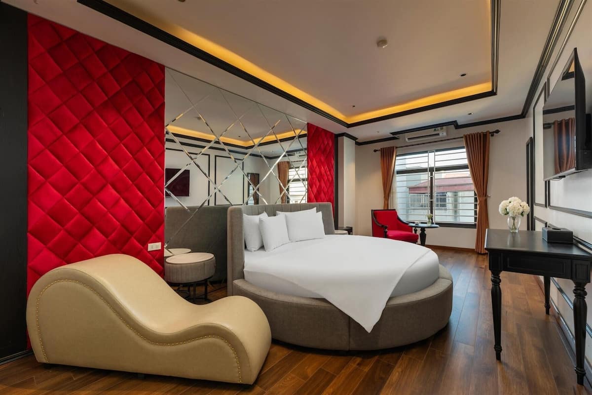 Ein modernes Hotelzimmer mit einem großen Bett, einer gebogenen Sitzgruppe und einer roten Akzentwand.