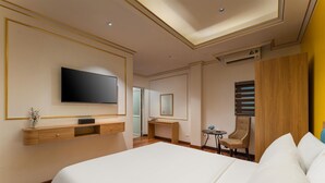 Ein Hotelzimmer mit einem großen Bett, einem an der Wand montierten Fernseher, einem Schreibtisch und einem Sessel.