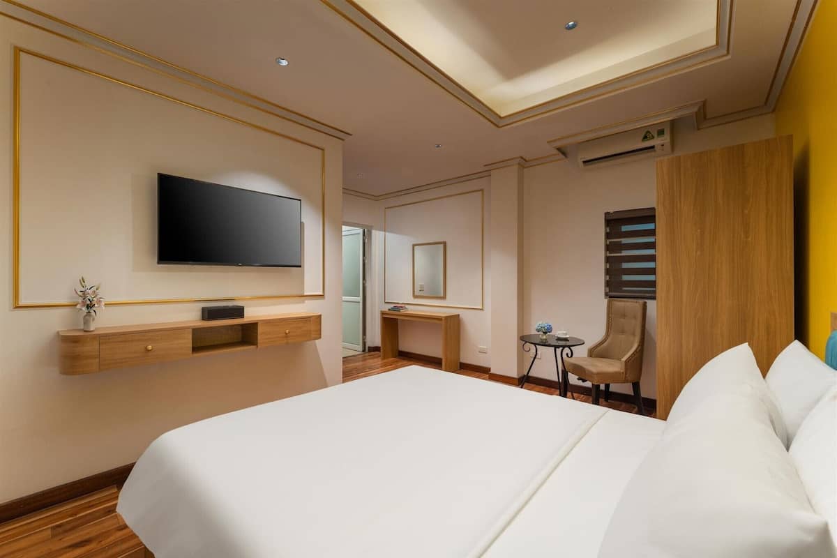 Ein Hotelzimmer mit einem großen Bett, einem an der Wand montierten Fernseher, einem Schreibtisch und einem Sessel.