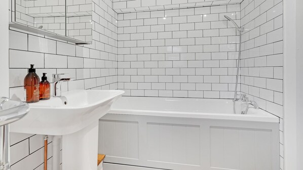 Un baño moderno con azulejos blancos tipo metro, un lavamanos blanco y una bañera.