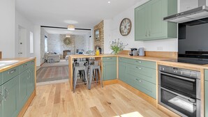 Een moderne keuken met groene kastjes, een houten aanrechtblad en roestvrijstalen apparatuur.
