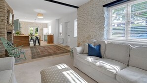Een woonkamer met een bank, een kamerbreed tapijt, een stenen muur en een raam met jaloezieën.