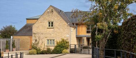 A stone building with a sloped roof, a gated entrance, and a small garden area.