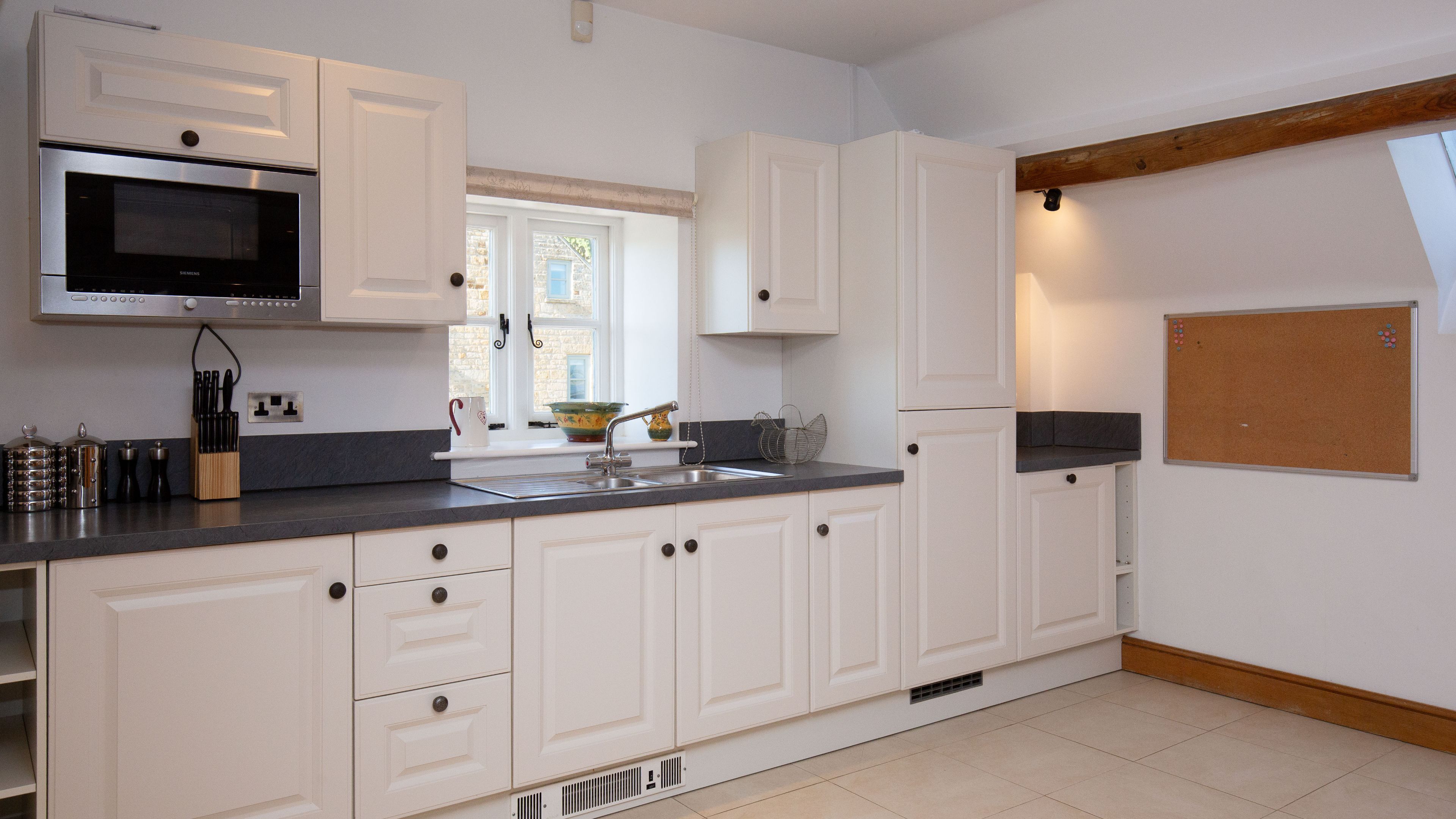 A modern kitchen with white cabinetry, a stainless steel microwave, and a window with a view of the outside.