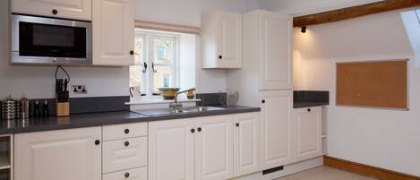 A modern kitchen with white cabinetry, a stainless steel microwave, and a window with a view of the outside.
