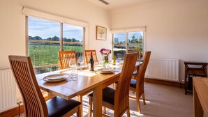 A dining room with a table set for four, large windows offering a view of a green field, and a radiator on the wall.