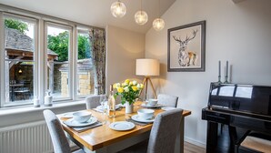 A dining area with a wooden table set for four, a piano, and a framed deer painting on the wall. - Old Orchard Cottage - Pet friendly, Moreton-in-Marsh (Moreton-in-Marsh)