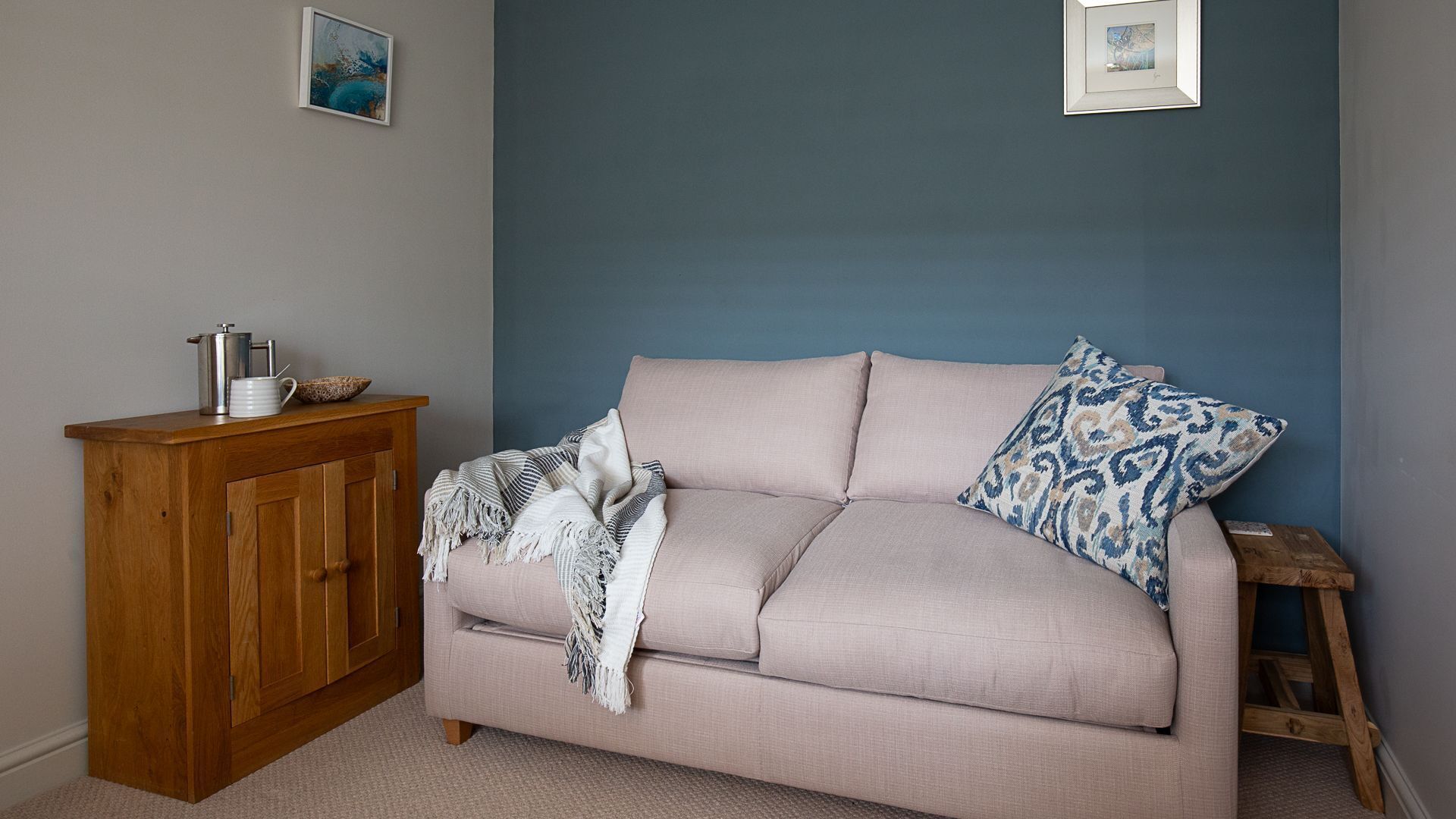 A room with a beige sofa, a wooden cabinet, and a blue wall.