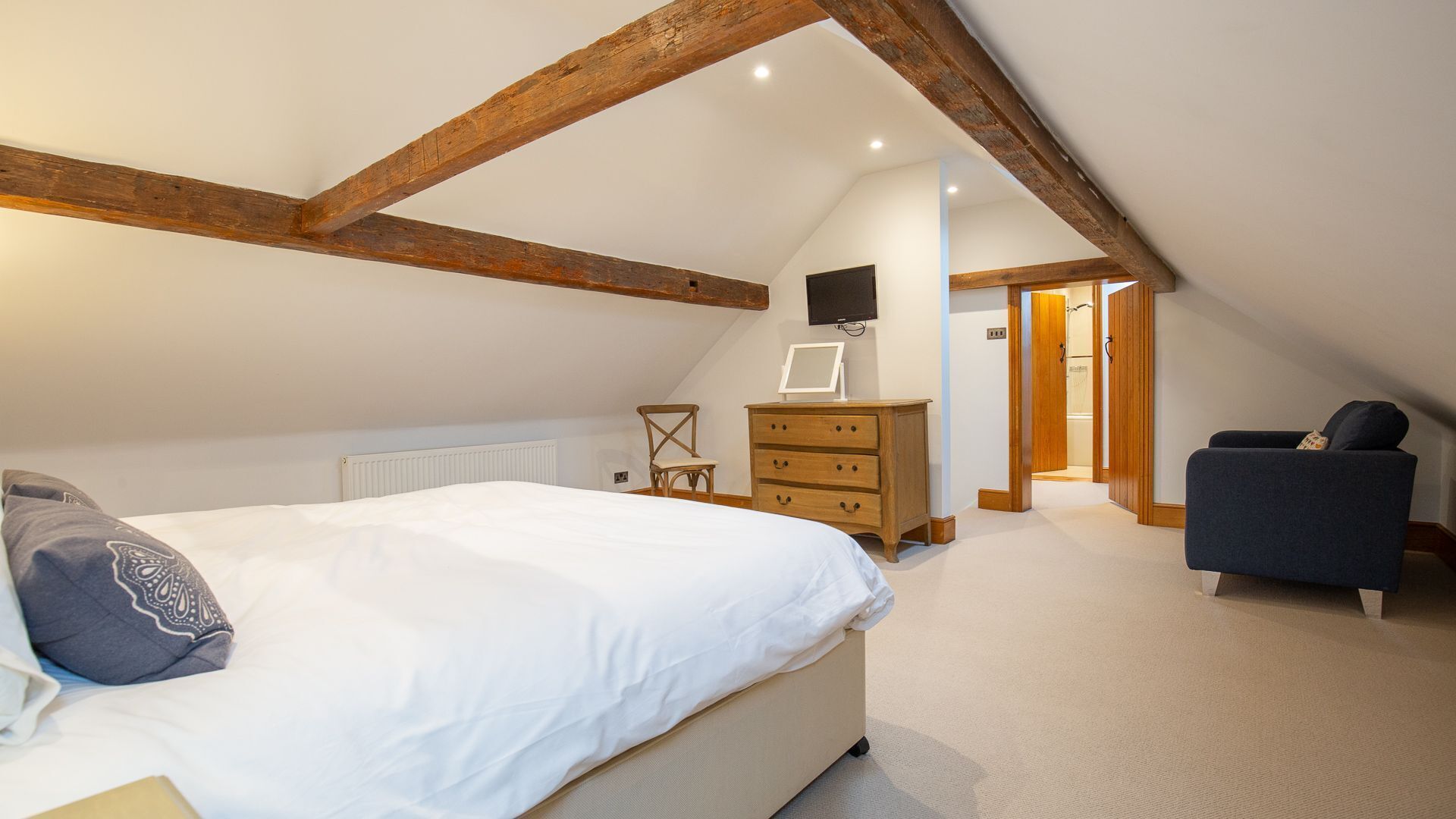 Een slaapkamer met een schuine kap, een bed, een dressoir, een stoel en een televisie aan de muur.