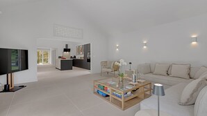 Ett modernt vardagsrum med en platt-TV, ett träbord med böcker, en soffa och en matplats med ett kök synligt i bakgrunden.