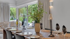 En matplats med ett långt bord dukat för en måltid, omgiven av stolar, och med utsikt över grönskan utanför.