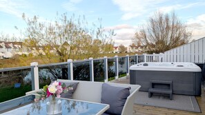 Een terras met een glazen tafel, rieten meubels en een hottub.