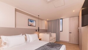 Ein modernes Hotelzimmer mit einem großen Bett, einer Couch, einem Fernseher und einem Kleiderschrank.