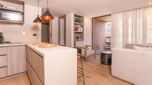 Een moderne keuken met een centraal eiland, houten kasten en hangende lampen. Er is een zithoek met een bank en een kleine tafel.