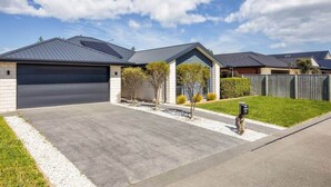 A residential property with a garage, a driveway, and a well-maintained lawn. - Silverstream Kaiapoi Retreat – 3BR Home with Spa & Sun-Filled Living (Kaiapoi)