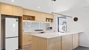 A modern kitchen with a built-in refrigerator, microwave, and stove. There is a large island with a sink and a clock on the wall. - Silverstream Kaiapoi Retreat – 3BR Home with Spa & Sun-Filled Living (Kaiapoi)