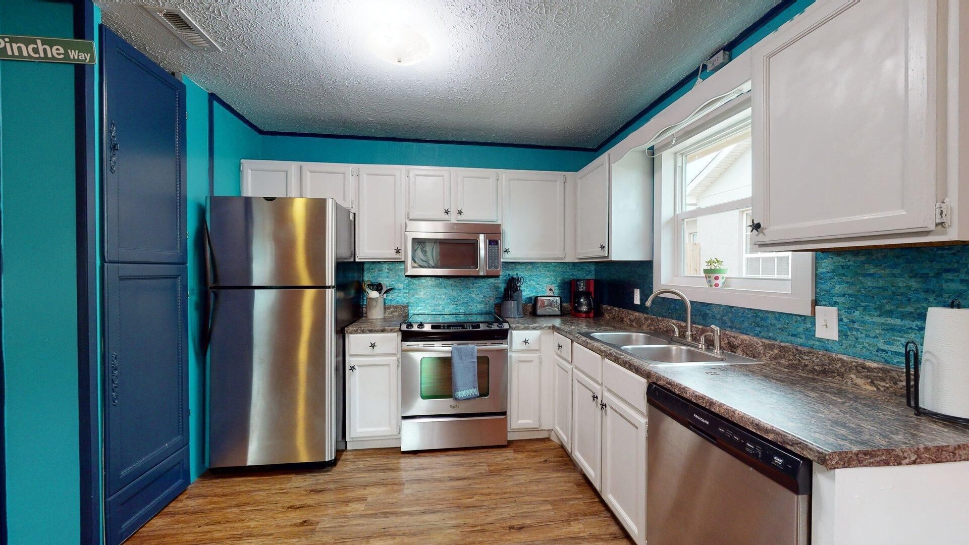 A kitchen with white cabinets, stainless steel appliances, a blue backsplash, and a wooden floor.