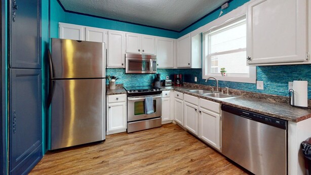 A modern kitchen with stainless steel appliances, white cabinets, and a blue backsplash. - Sunset Ave Beach House - Golf Cart Pool Hot Tub (Panama City Beach)