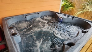 A hot tub with a stone exterior, surrounded by wooden decking and a wooden fence. - Sunset Ave Beach House - Golf Cart Pool Hot Tub (Panama City Beach)