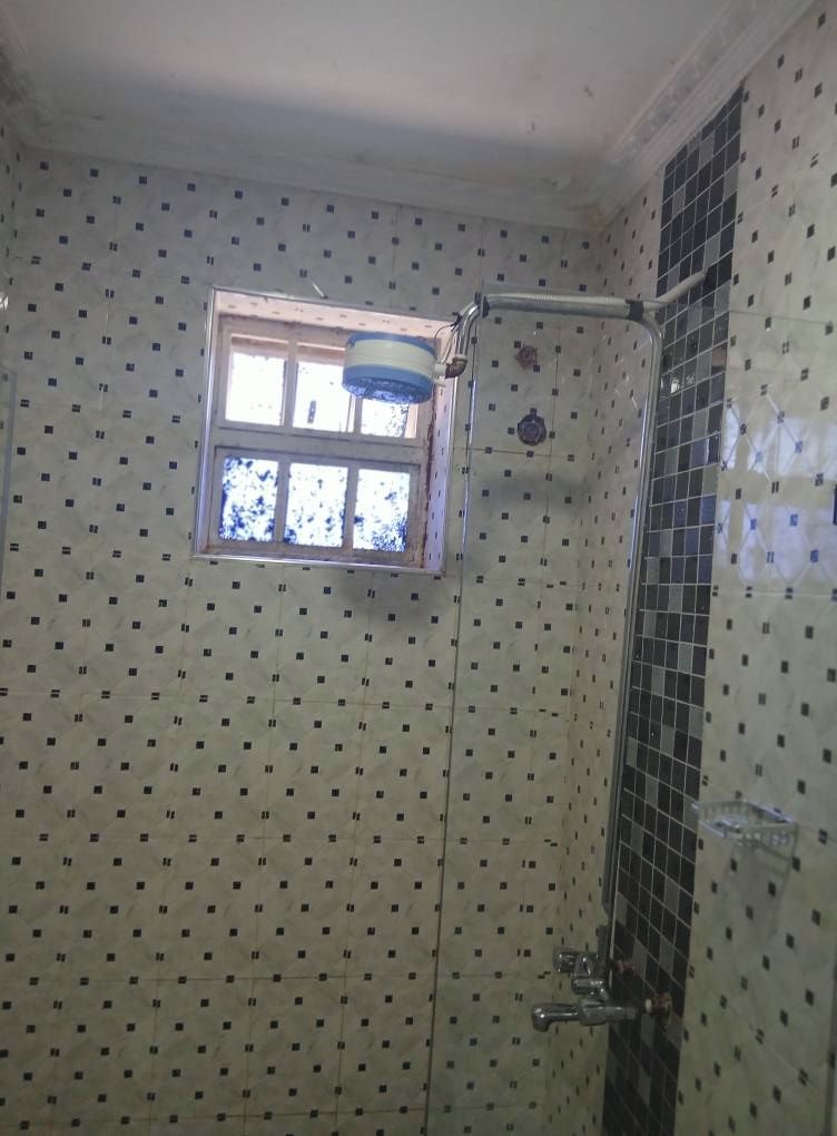 A bathroom with a tiled wall, a window, and a shower area.