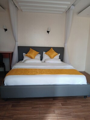 Uma cama de casal com cabeceira cinza, roupa de cama branca e duas almofadas douradas.
