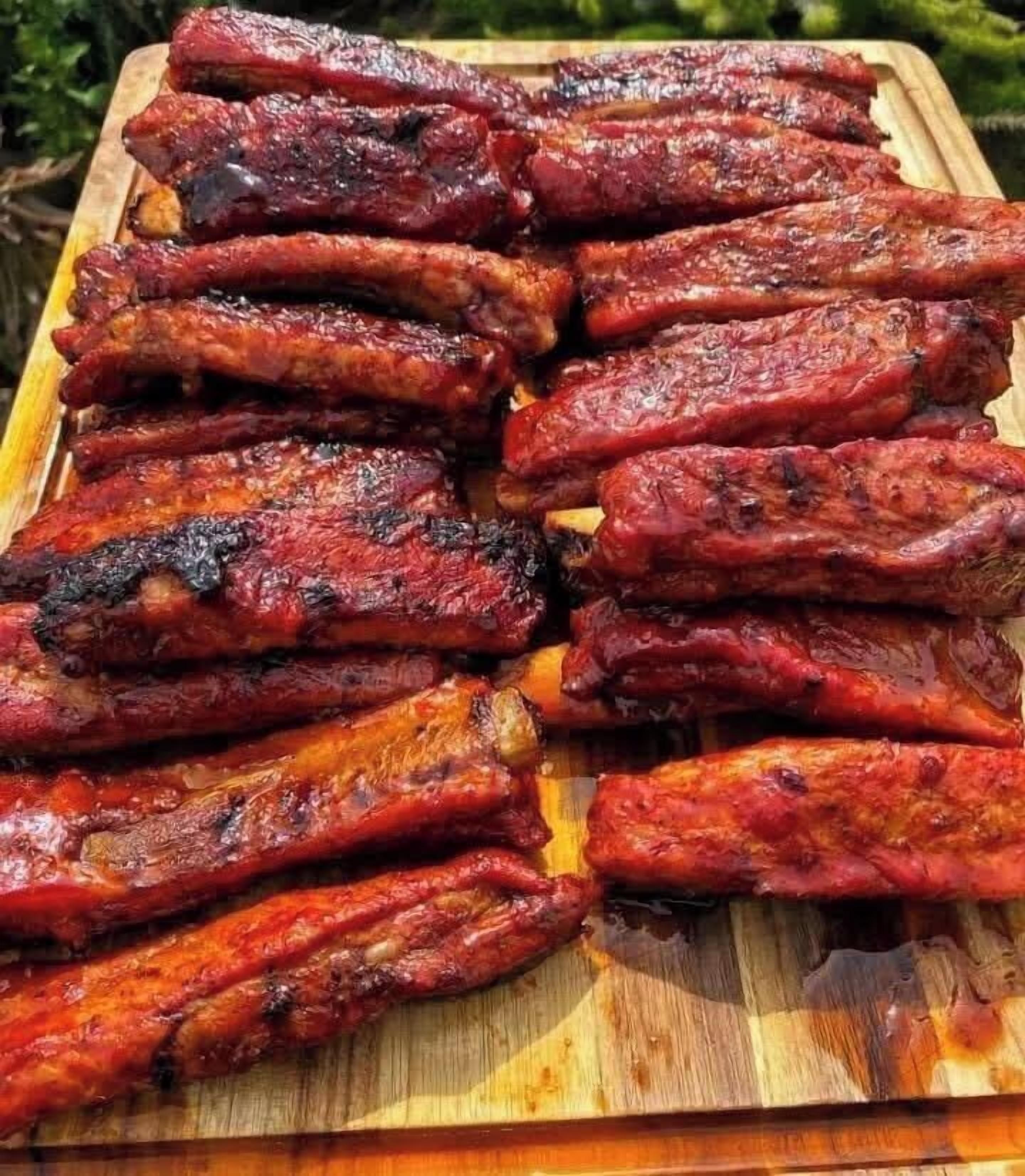 A wooden cutting board with several grilled ribs arranged on it.
