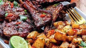 Une assiette de côtelettes d’agneau grillées et de pommes de terre rôties, garnie d’herbes et de citron vert.