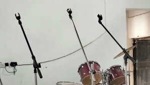 Une pièce avec une batterie et deux pieds de microphone, le tout posé sur un sol carrelé.