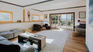 A modern living room with a sofa, coffee table, and a view through a glass door to an outdoor patio. - Lyon Mountain Lodge (Saranac)