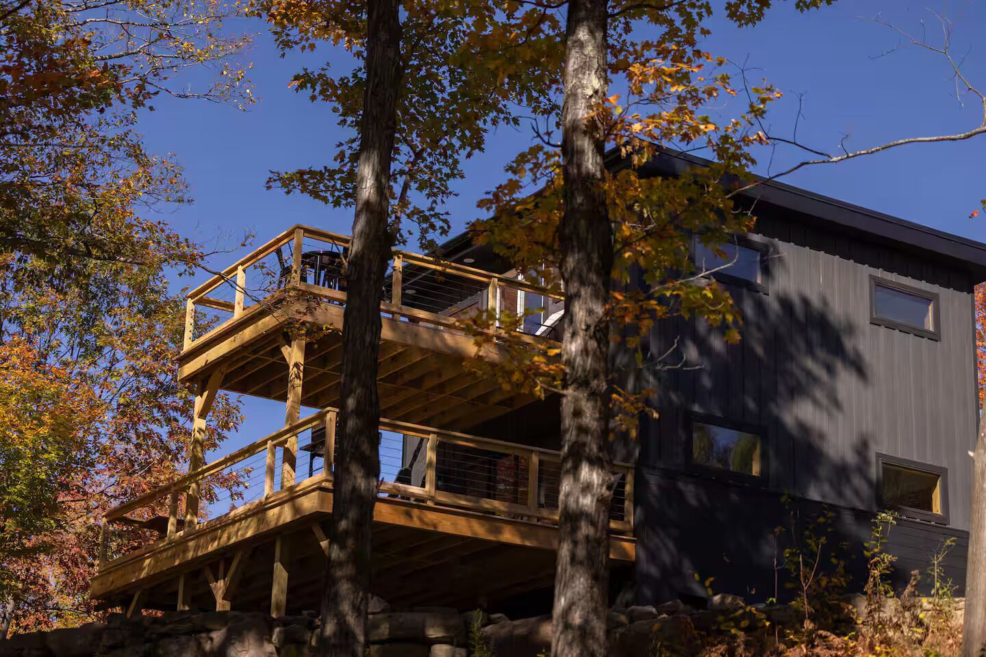 A two-story wooden cabin with a balcony, surrounded by trees.