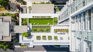 Vista aérea de un edificio moderno con jardín en la azotea, varias terrazas y un estacionamiento.